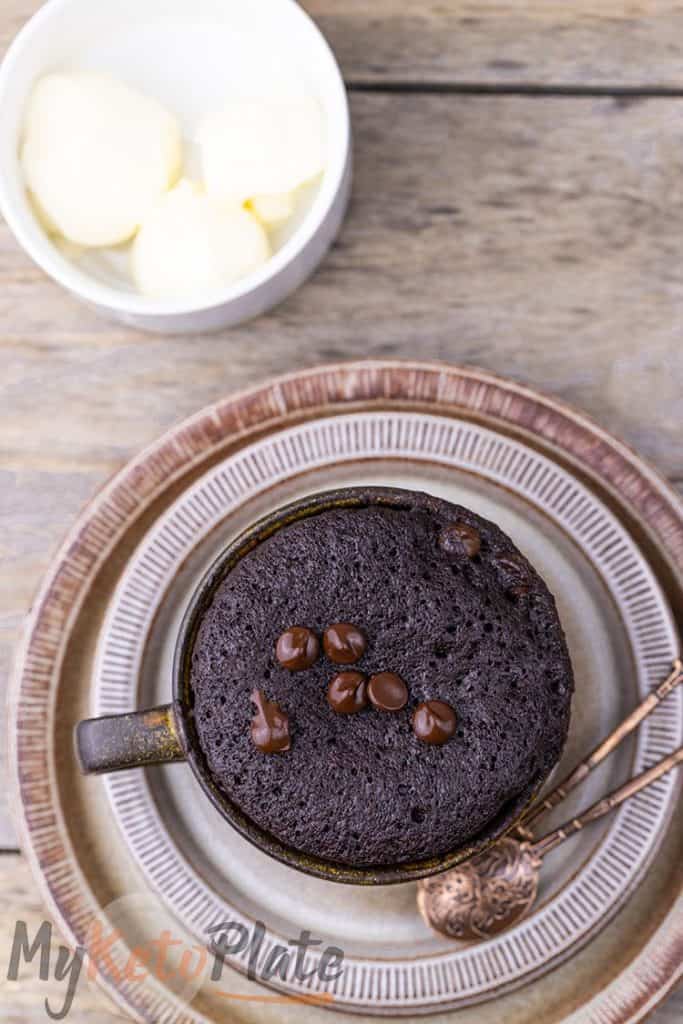 Warm chocolate mug cake in a brown stoneware cup, with a ramekin of sugar‑free ice cream waiting to be added.