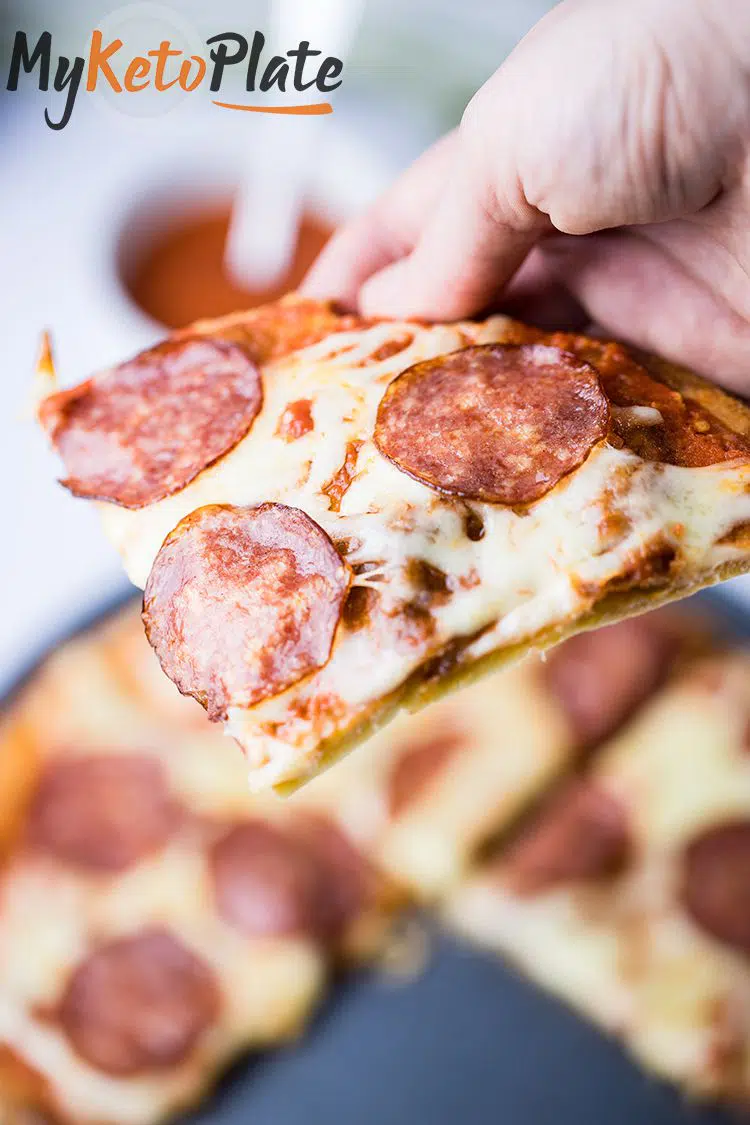 keto pizza slice hold in a hand that is ready to enjoy