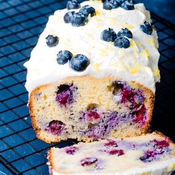 a whole loaf of low carb blueberry bread topped with cream cheese frosting and blueberries on a black background