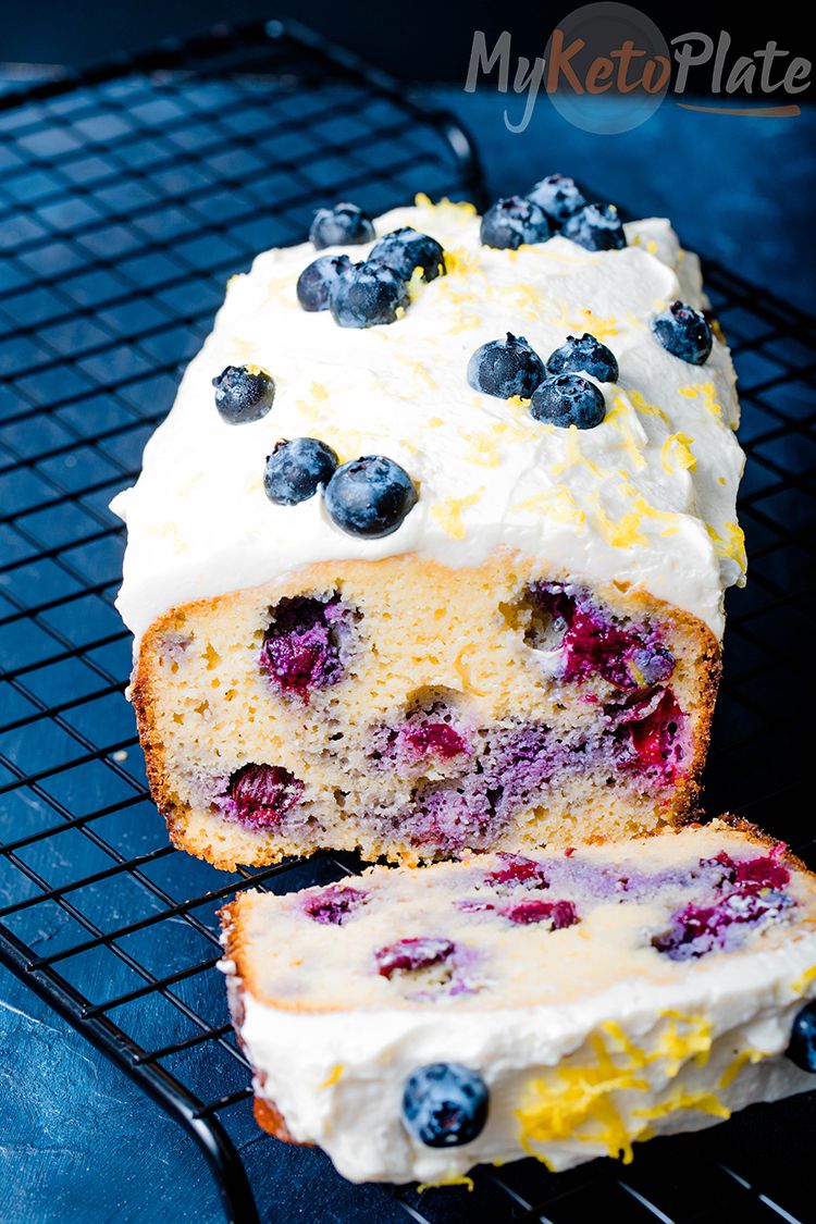a whole loaf of low carb blueberry bread topped with cream cheese frosting and blueberries on a black background