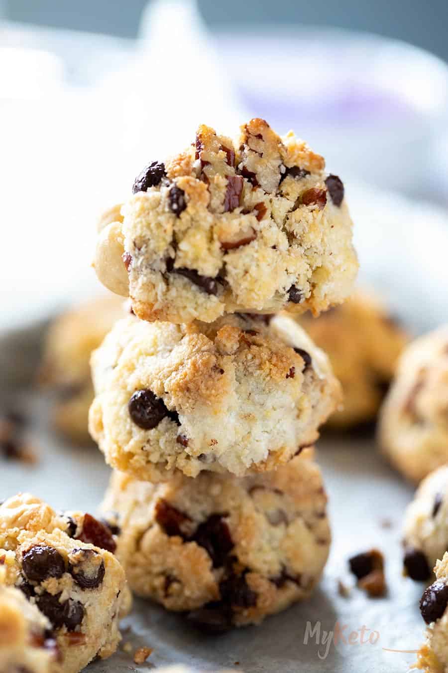 A stack of homemade keto cookies with chocolate chips and nuts on a parchment-lined surface.
