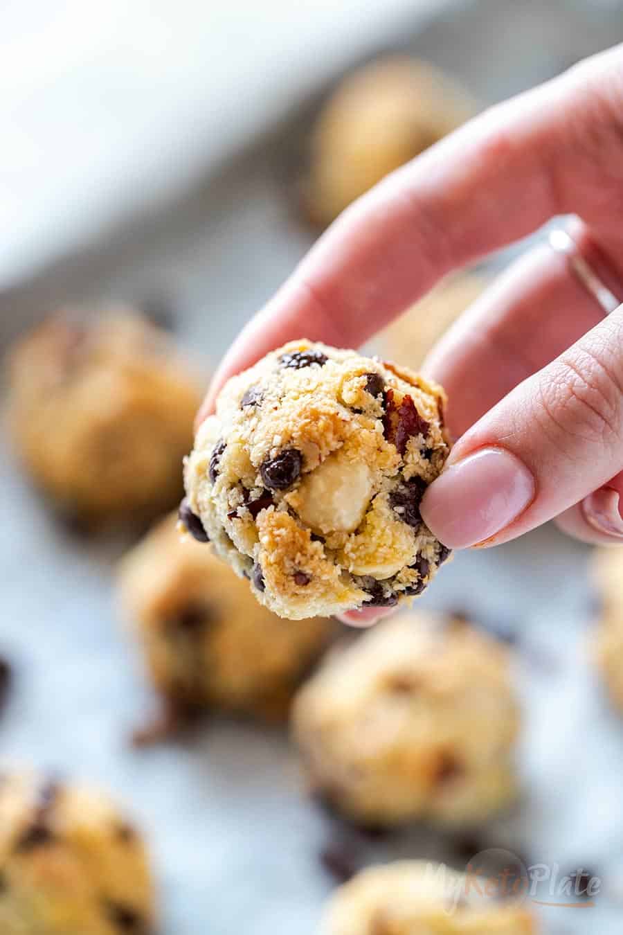 A soft, chewy keto cookie with crisp edges, held between two fingers.