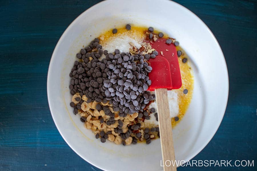 A bowl of keto cookie ingredients, including chocolate chips, coconut, and chopped nuts.