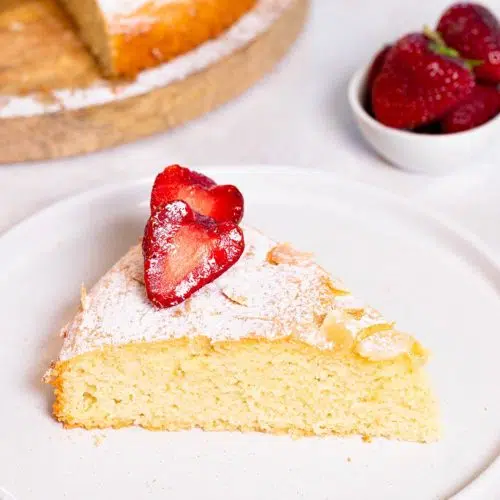 A single slice of gluten-free almond cake with a tender crumb, decorated with sliced almonds and powdered sugar.