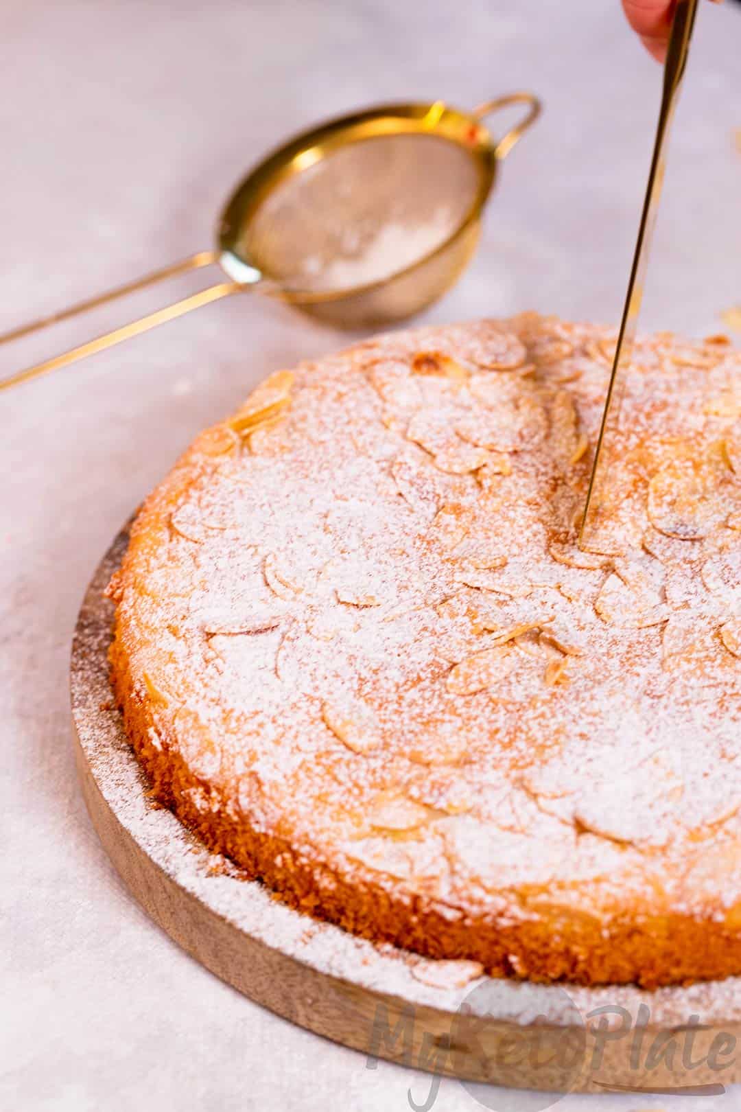 Cutting into a keto almond cake, showing its delicate crumb and lightly toasted almond topping.
