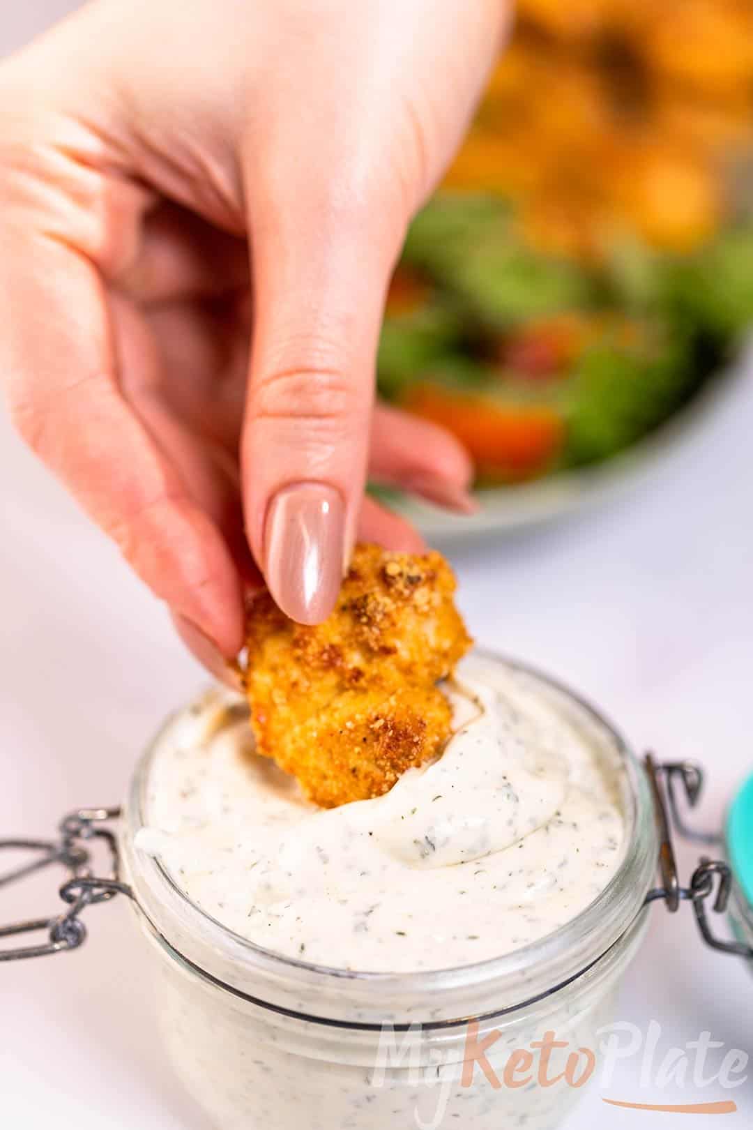 A crispy chicken nugget being dipped into thick keto ranch dressing.