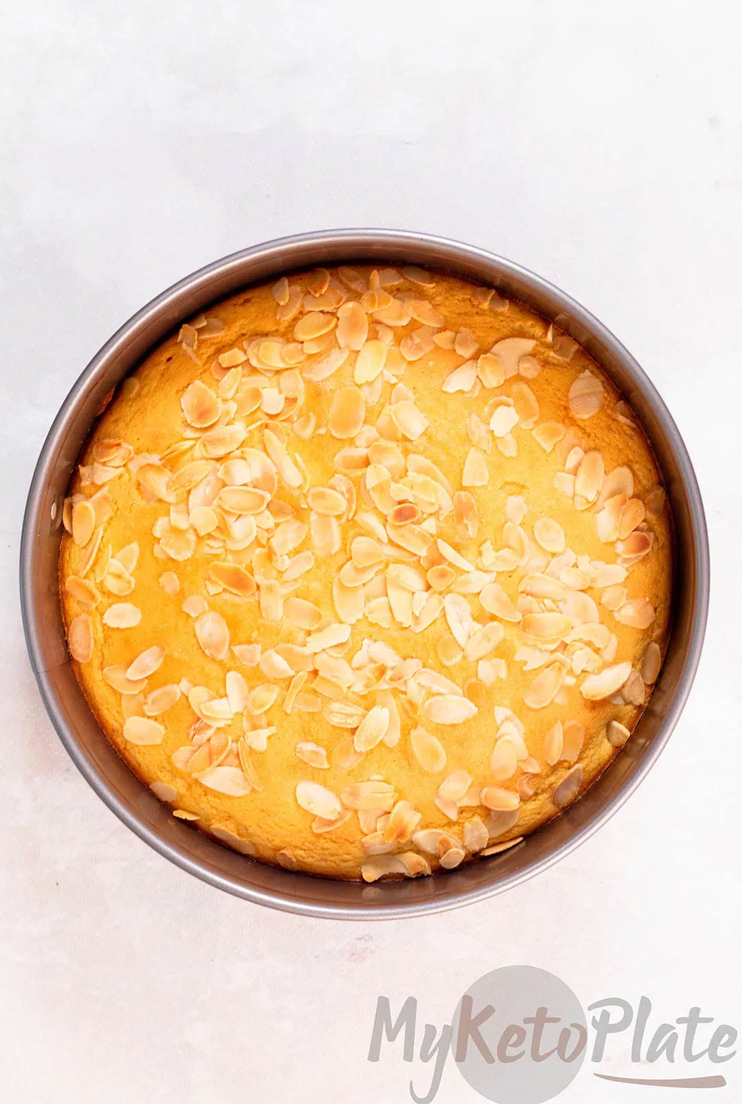 A freshly baked almond flour cake in a round pan, topped with golden sliced almonds.
