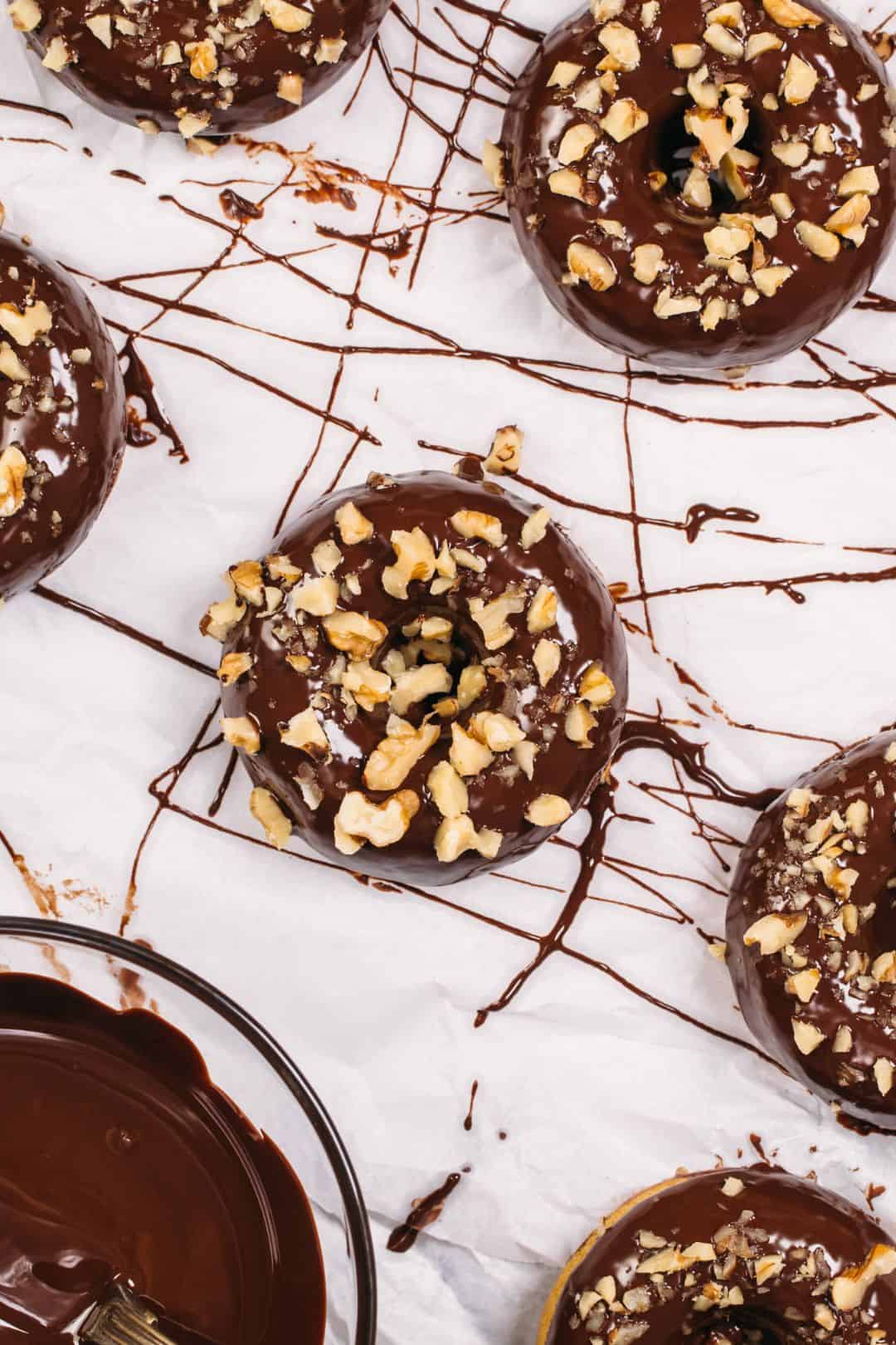 Keto donuts coated with rich chocolate glaze and sprinkled with chopped nuts.
