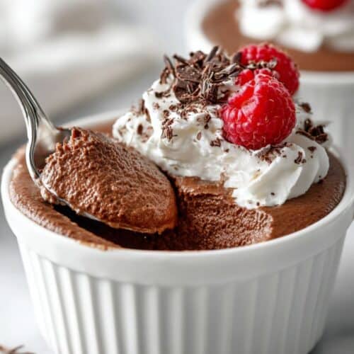 Close-up of velvety chocolate mousse showing its texture as a spoon lifts a bite beneath whipped cream and fresh berries.