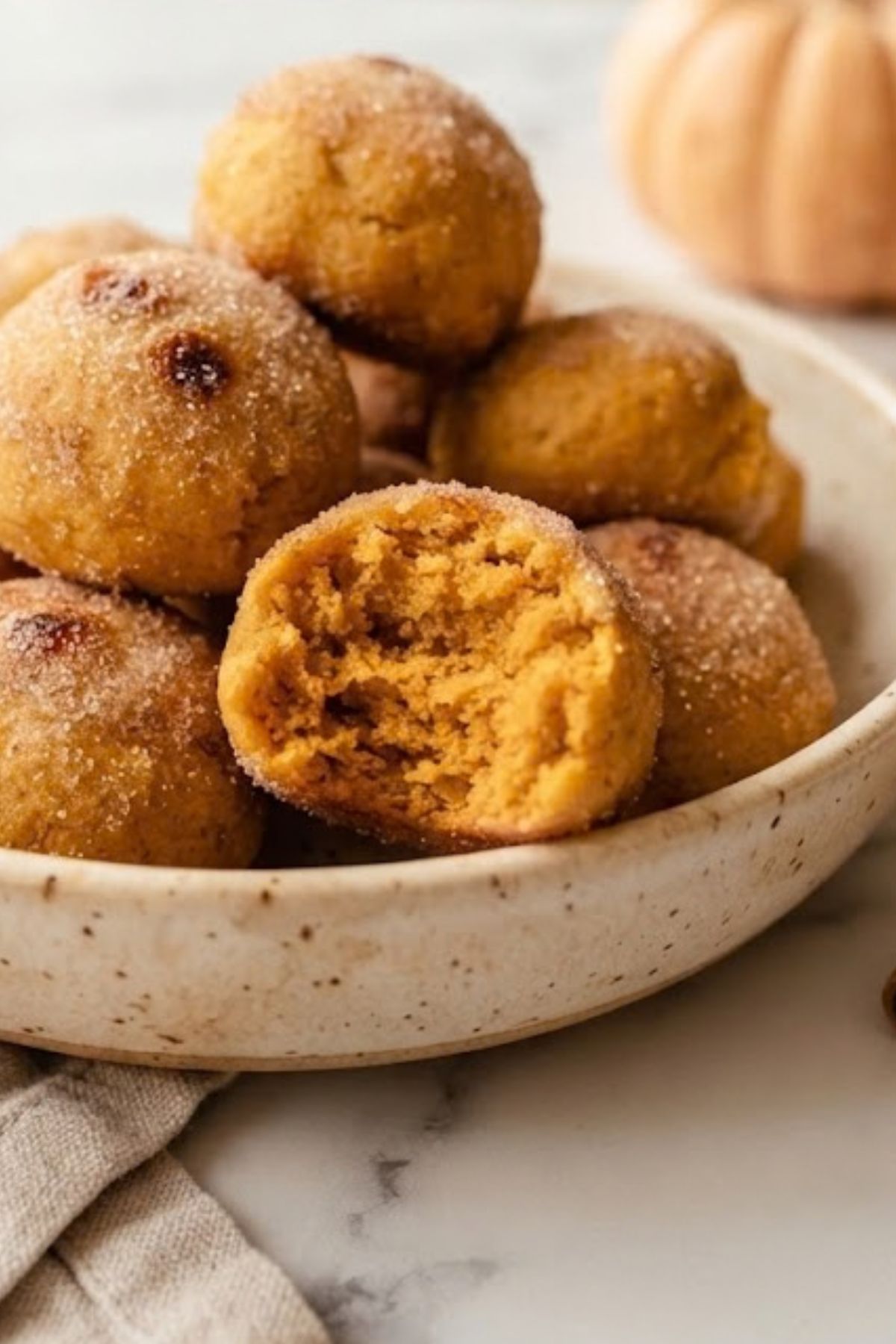 Almond Flour Pumpkin Donut Holes 4 Close-up of Easy Baked Pumpkin Donut Holes coated in cinnamon sugar, with one broken open to show the soft pumpkin center.