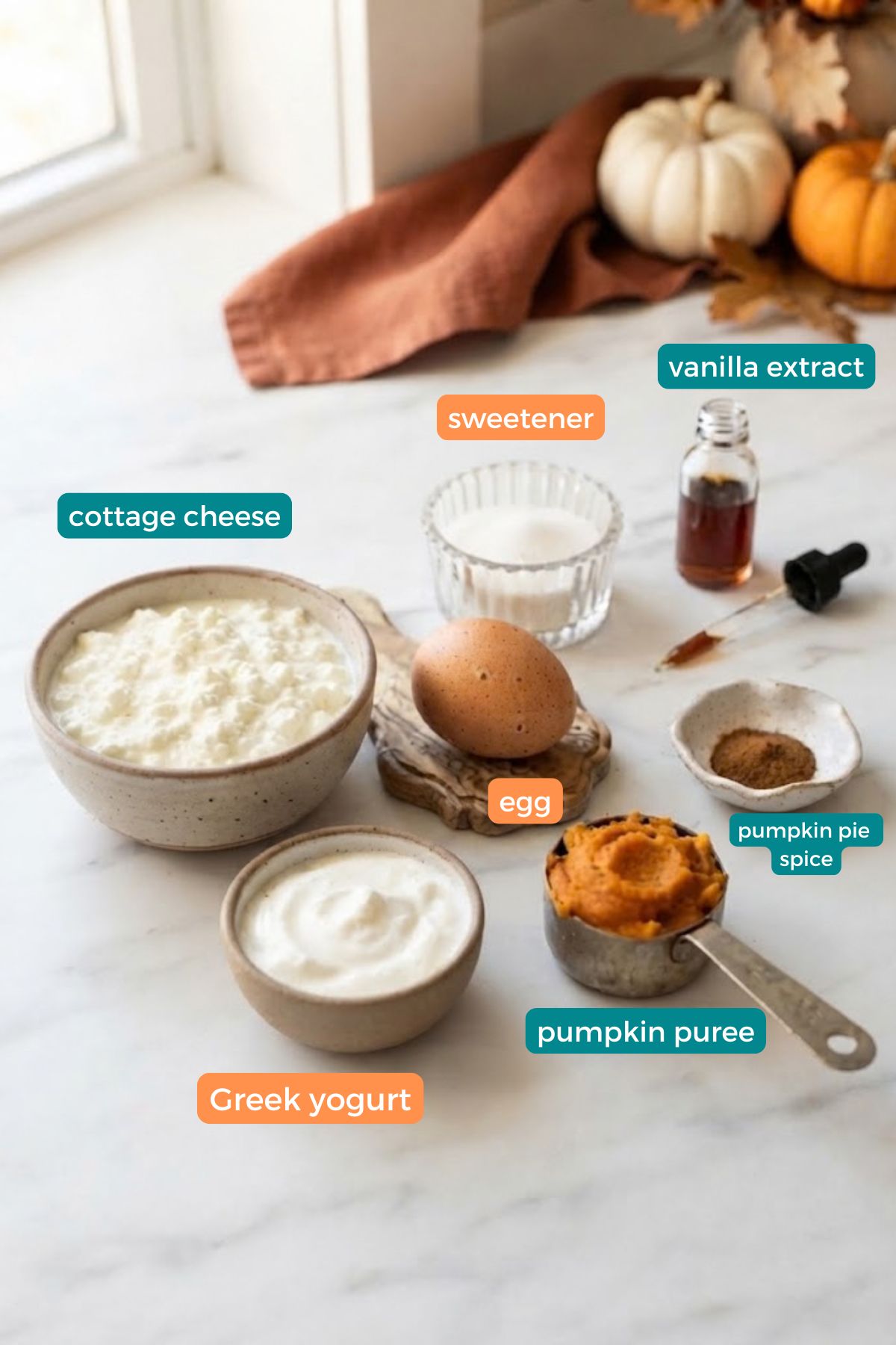 High-Protein Cottage Cheese Pumpkin Cheesecake 4 Ingredients for High-Protein Cottage Cheese Pumpkin Cheesecake arranged on a marble counter, including cottage cheese, Greek yogurt, pumpkin purée, egg, vanilla, and cinnamon.